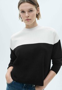 Black and white color-block sweater with a round neckline, ribbed cuffs, and soft knit texture, worn over blue jeans.