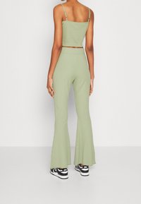 Ribbat, ljusgrön tvådelad outfit som består av en cropped topp med tunna axelband och utsvängda byxor med en texturerad yta, tillsammans med svarta sneakers.