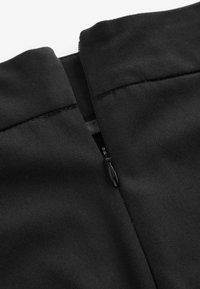 Gros plan d'une fermeture éclair noire partiellement ouverte sur un tissu noir texturé, montrant les détails de couture le long des bords.
