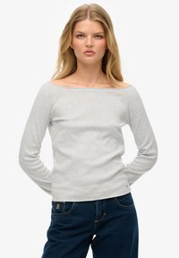 Graues Langarm-Oberteil mit schulterfreiem Schnitt aus weicher Baumwolle, das ein einfaches Design und eine figurbetonte Silhouette aufweist, kombiniert mit dunkelblauen Jeans.