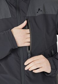 Svart jacka med en tvåfärgad design och en mjuk textur, främre dragkedja och justerbara manschetter, som visar en utilitaristisk stil.