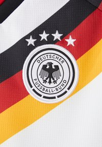 Blason de l'équipe nationale de football allemande avec quatre étoiles au-dessus, sur un fond de maillot blanc avec des rayures diagonales noires, rouges et jaunes.