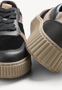 Black and beige platform sneakers featuring a mix of leather and suede materials, textured ribbed sole, and flat rounded laces.