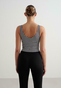 Juodai balta houndstooth rašto palaidinė su giliu nugara; derinama su juodomis prisitvirtinančiomis tamprėmis. Lygus audinys, paprastas dizainas.