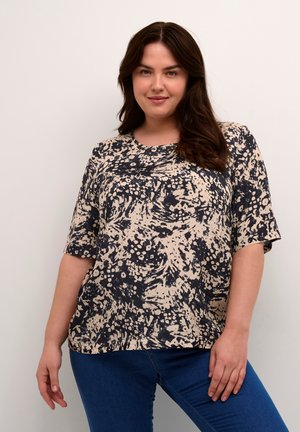 Top ampio con una stampa astratta beige e nera, maniche corte, scollatura tonda e texture morbida. Abbinato a jeans blu.