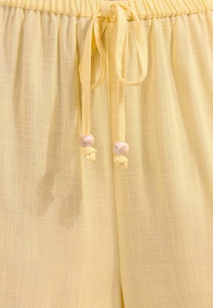 Gule lette bukser med elastisk talje og snørebånd, der ender i runde, marmoragtige perler.