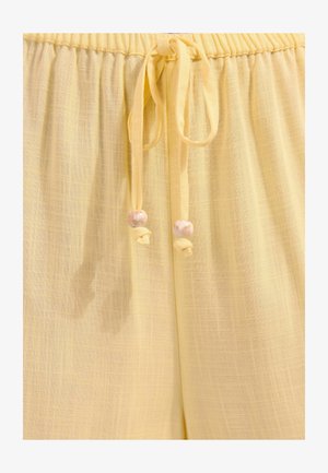 Gelbe leichte Stoffhose mit elastischem Bund und Kordeln, die in runden, marmorierten Perlen enden.