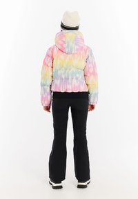 Farebná nafukovacia bunda s pastelovým batikovaným vzorom, s kapucňou, elastickými manžetami a priliehavým strihom. Nosená over čiernymi nohavicami a topánkami.