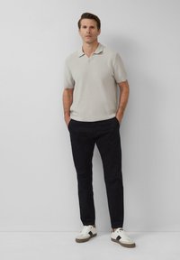 Polo shirt gris clair texturé à manches courtes associé à un pantalon bleu marine et des baskets blanches avec des accents bruns.