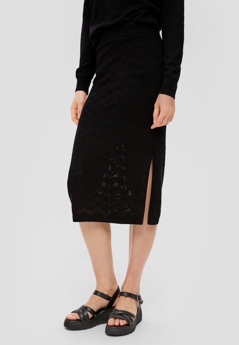 Jupe midi tricotée noire avec un motif en chevron, une fente sur le côté et une taille côtelée, associée à des sandales noires à lanières.