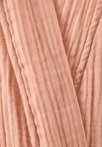 Tissu texturé de couleur pêche avec une surface froissée et des rayures verticales, révélant un matériau doux et respirant.