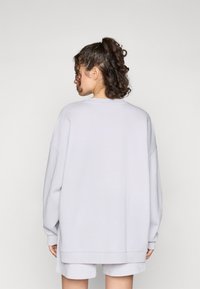 Sweatshirt oversize gris clair avec un col rond et des épaules tombantes, doté de poignets et d'un ourlet côtelés, en tissu en coton doux.