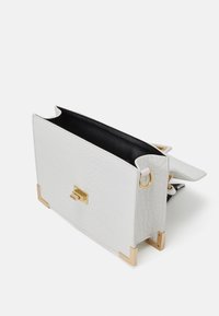 Sac en cuir blanc texturé avec intérieur noir, accents dorés aux coins, et forme rectangulaire. Dispose d'un mécanisme de fermeture simple.