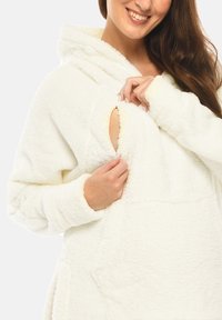 White, plush fleece hoodie with a large front pocket and a cutout detail. Features a cozy hood and thick sleeves for warmth.
