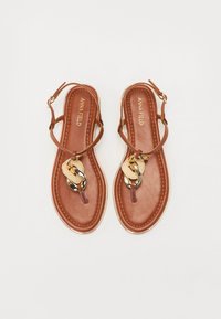 Sandalias de cuero marrón con suela plana, que presentan un diseño de tiras delgadas y un acento decorativo de cadena dorada en el centro.