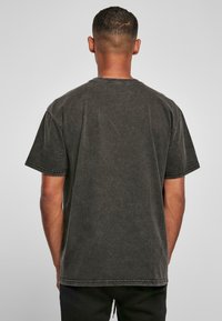 Mørkegrå bomulds T-shirt med korte ærmer og rund halsudskæring, med en falmet tekstur og synlige sømdetaljer ved kanten.