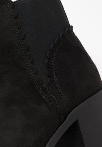 Czarne zamszowe botki za kostkę z falistymi akcentami, elastycznymi panelami bocznymi i masywnym obcasem. Gładka tekstura o matowym wykończeniu.