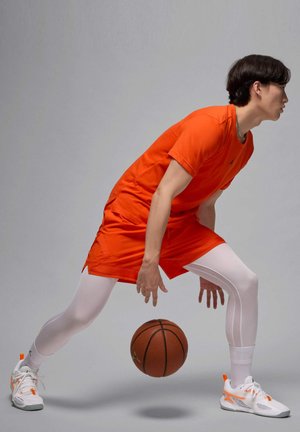 Pomarańczowa sportowa koszulka i spodenki z białymi legginsami, trzymając koszykówkę. Buty są białe z pomarańczowymi akcentami i szczegółową teksturą.