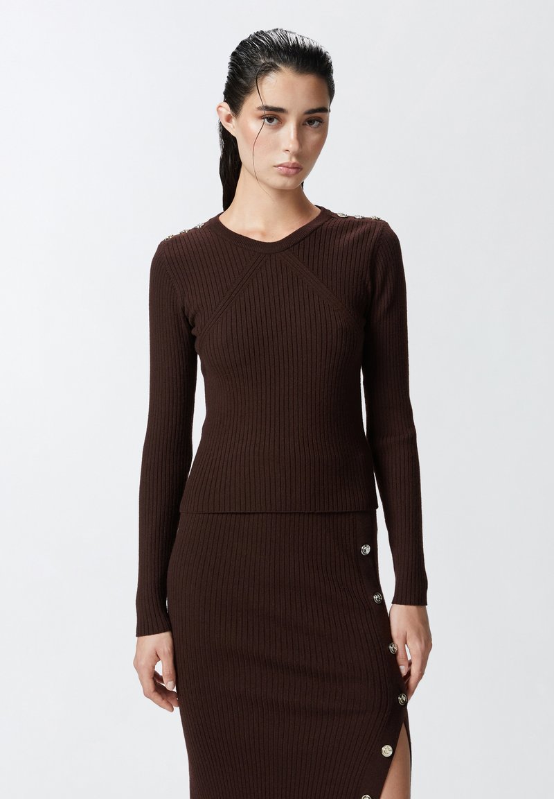 Top lungo a maniche con costine marrone, dalla silhouette aderente, con bottoni decorativi sulla spalla e scollo a girocollo.