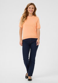 Pull court orange clair à manches courtes avec un col rond, associé à un jean droit bleu marine et des ballerines noires.