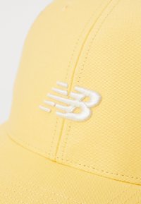 Yellow cap with embroidered white logo. Features textured fabric, curved brim, and a stitched seam along the front panel.