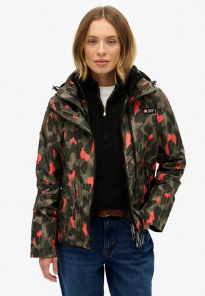 Veste camouflage en vert olive avec des accents rouges. Dotée d'une fermeture éclair à l'avant, d'un col montant et de plusieurs poches. Fabriquée en matériau résistant aux intempéries.