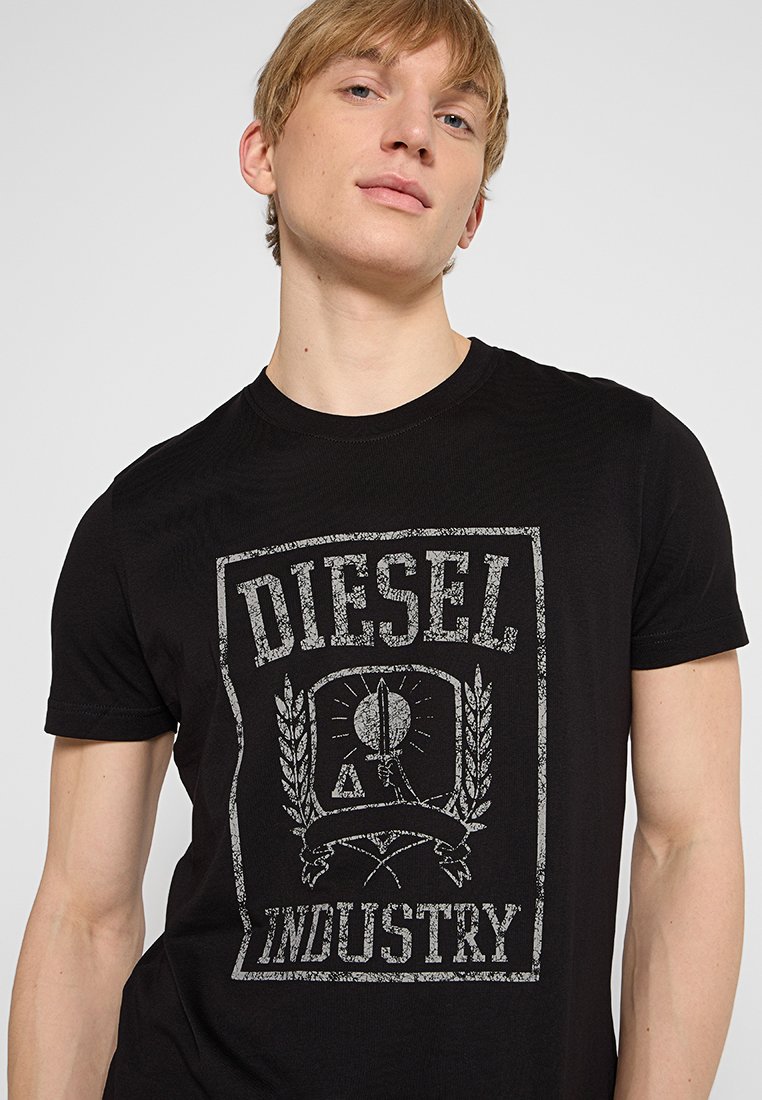 T-shirt en coton noir avec un imprimé graphique argenté usé portant le texte "DIESEL" et "INDUSTRY", entouré de branches de laurier.