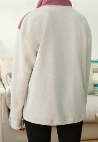 Polarowy pulower w jasnoszarym kolorze z różowym kołnierzem i akcentami na ramionach. Posiada luźny krój oraz boczny sznurek do regulacji.