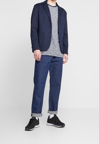 Námořnický blazer, šedé pruhované tričko, modré džíny po kotníky a černé tenisky. Mezi rysy patří kapsy na blazeru a ohrnuté džíny.