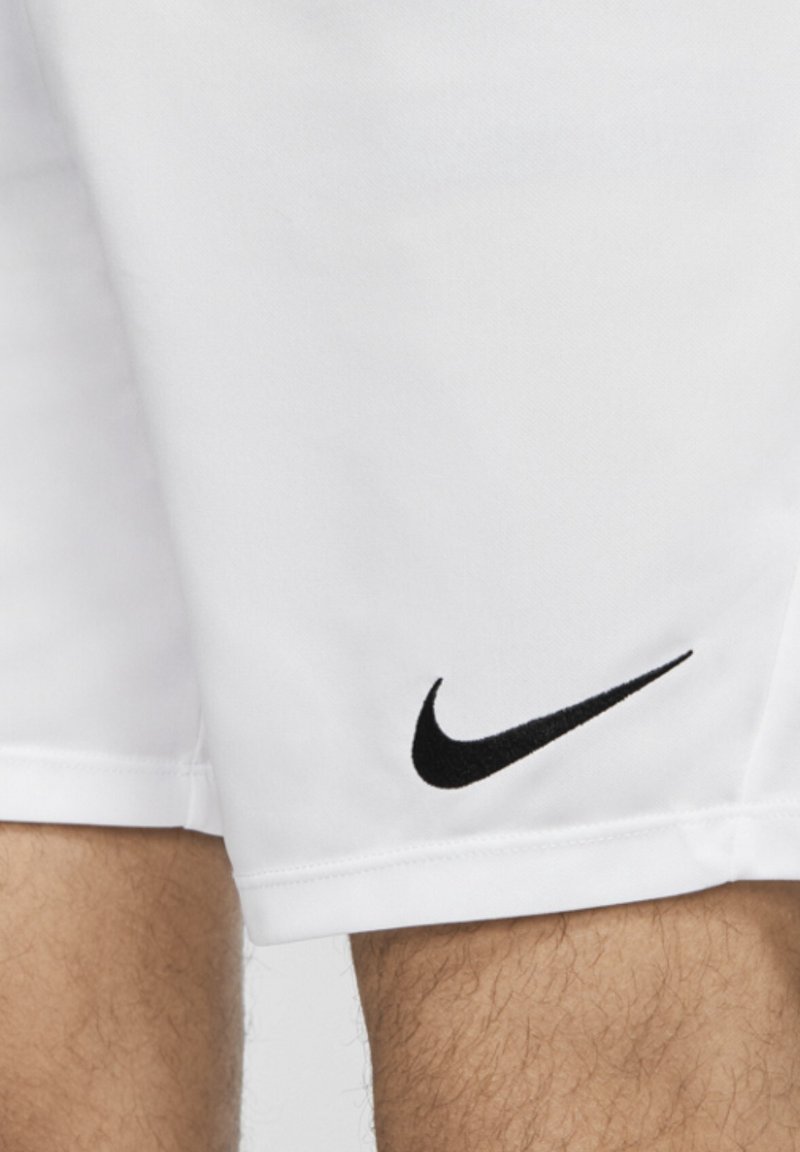 Shorts de sport blancs portés sur les jambes avec un logo Nike swoosh noir près de l'ourlet côté gauche.