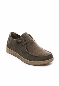 Zapatos de lona marrones con un diseño slip-on, cordones elásticos y suela de goma. Presentan una textura suave y un logo sutil en el lateral.