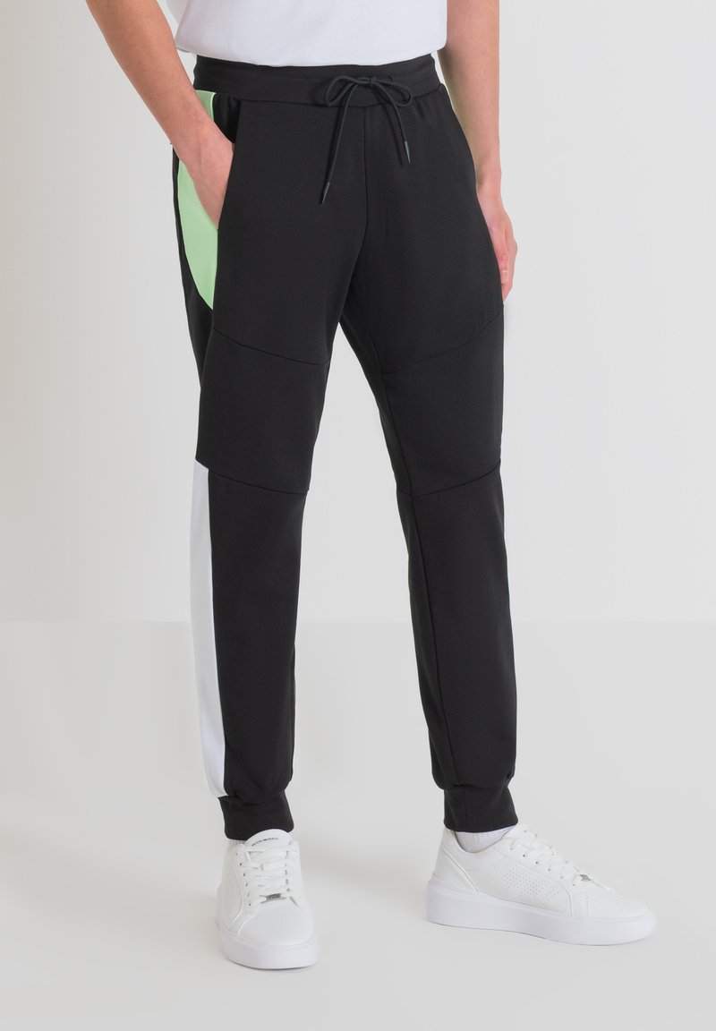 Zwarte joggers met groene en witte accenten aan de zijkanten, trekkoord in de taille, elastische boorden en zijzakken. Gemaakt van zachte, lichte stof.