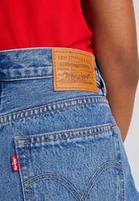 Vaqueros de mezclilla azul de Levi's con una parche de cuero marrón etiquetado "Levi Strauss & Co." y costuras naranjas, que presentan un diseño característico en el bolsillo trasero.