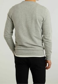 Maglione grigio lavorato a maglia con maniche lunghe e scollo rotondo, presenta una texture sottile e orlo a coste, indossato sopra una camicia bianca.