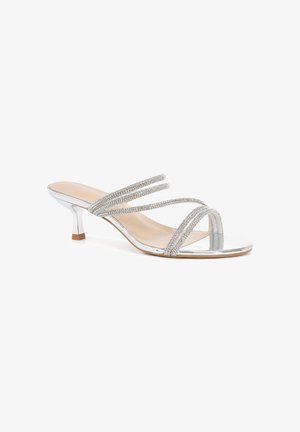 Sandalo argento con punta aperta e tacco basso, con quattro sottili cinturini con strass sul piede e soletta beige su sfondo bianco.