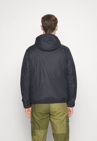 Marineblaue Pufferjacke mit Kapuze, gestepptem Design, elastischen Bündchen und lockerer Passform, kombiniert mit olivgrünen Cargo-Hosen.