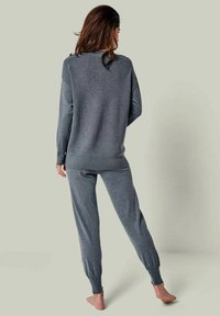 Grau gestricktes Loungewear-Set mit einem langärmeligen Oberteil und tapered Hosen mit gerippten Bündchen, präsentiert vor einem hellgrünen Hintergrund.