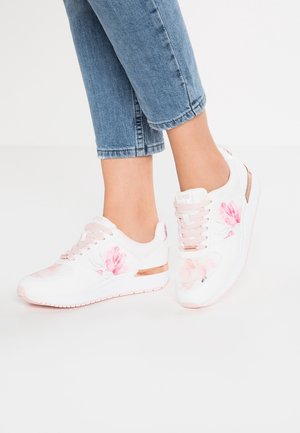 Hvide sneakers med lyserøde blomsterprint og lyserøde snørebånd, båret med blå cropped jeans på en lys baggrund.