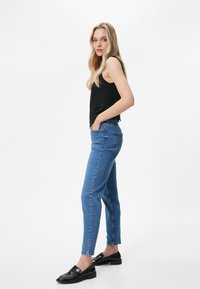 Blå denimjeans med en figursydd design. Bärs med en svart ärmlös topp och svarta loafers. Slät textur och midjehögt skär.