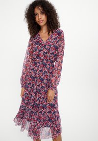 Blumenkleid mit navy Hintergrund, das rote und rosa Blumen zeigt, lange durchsichtige Ärmel, einen V-Ausschnitt und einen gestuften, rüschengesäumten Saum hat.