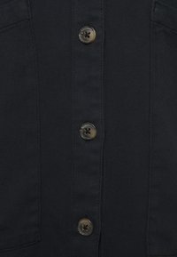 Chemise en denim bleu foncé au design droit, dotée de cinq boutons en métal, de deux poches poitrine et d'un tissu légèrement texturé.