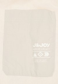 Lichtgrijze stoffen zak met witte afgedrukte tekst en geometrische ontwerpen. De tekst luidt: "J&Joy Andean Legacy" en "Vanuit het Hart van Zuid-Amerika."
