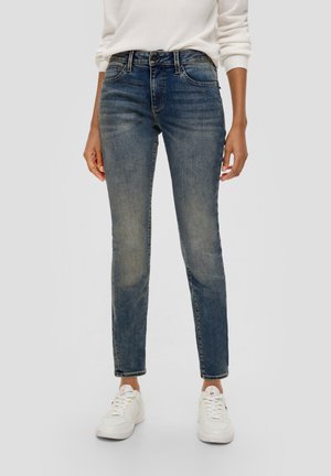 Dark blue denim jeans with a slim fit, five pockets, subtle fading, and a standard waistband, paired with white sneakers.