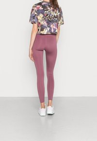 Avskuren blommig topp i nyanser av lila, rosa och krämig, kombinerad med åtsittande vinröda leggings och vita sportskor.