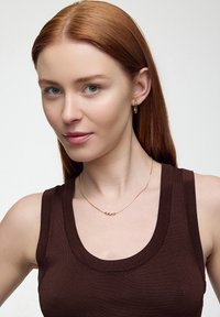 Złoty naszyjnik z trzema okrągłymi koralikami, noszony na brązowej bluzce bez rękawów. Gładka faktura, minimalistyczny design, delikatny łańcuszek.