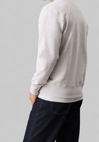 Sudadera gris con puños y dobladillo acanalados, tejido ligero, vista desde atrás, combinada con jeans de mezclilla oscura.