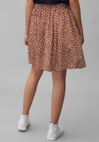 Gonna marrone a fantasia con un design a pois bianchi, vita elastica e tessuto plissettato. Abbinata a stivaletti bianchi alla caviglia.