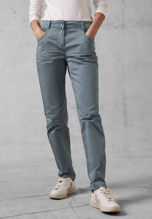 Light blue, slim-fit pants with two front pockets and a zip fly, featuring stitched detailing and a smooth texture. Paired with white sneakers.