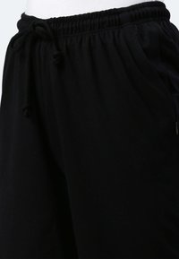 Schwarze Jogginghose aus weichem Material, mit einem elastischen Bund und Kordelzug, seitlichen Taschen und einem lockeren Schnitt.