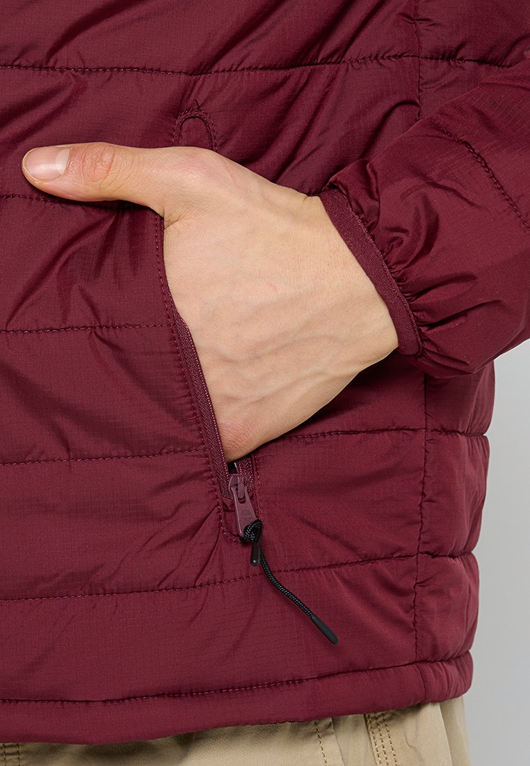 Giacca isolante bordeaux con texture trapuntata, dotata di tasca laterale con zip e polsini elasticizzati per una vestibilità aderente.